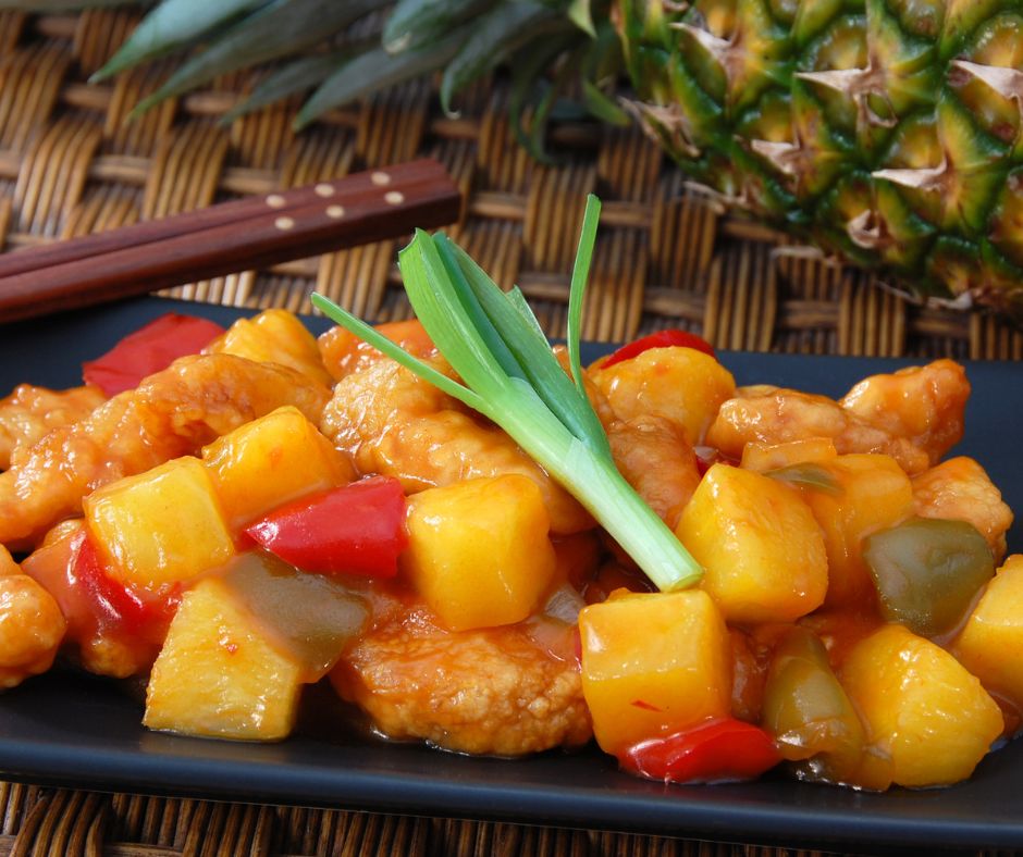 Un atractivo plato de pollo agridulce con infusión de piña, adornado con coloridos pimientos y suculentos trozos de piña.